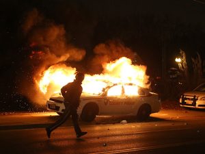 FERGUSON, MO - NOVEMBER 24: A police officer runs by a burning police car during a demonstration on November 24, 2014 in Ferguson, Missouri. A St. Louis County grand jury has decided to not indict Ferguson police Officer Darren Wilson in the shooting of Michael Brown that sparked riots in Ferguson, Missouri in August. (Photo by Justin Sullivan/Getty Images)